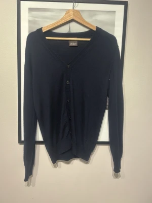 Mörkblå cardigan från Oscar Jacobson - Klassisk mörkblå cardigan från Oscar Jacobson med v-ringning och knäppning framtill. Tröjan har långa ärmar och ribbade muddar vid ärmslut och nederkant. Perfekt för lager-på-lager och stilrena outfits.pris kan diskuteras!!!😁 använd ca 2 gånger efter som den blev förliten 