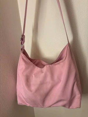 Rosa axelväska carry bag Weekday - Säljer denna superfina rosa axelremsväska/ cross body bag från Weekday! 🩷 Väskan är hel och utan hål osv men fläckar förekommer, främst på baksidan, därav ett lägre pris. Jag har inte försökt ta bort fläckarna och väskan säljes i befintligt skick, så mycket möjligt att de går bort vid en tvätt.   Mått:  Bredd: 45 cm Djup: 8 cm Höjd: 26 cm   Skicka ett meddelande vid frågor! 😊