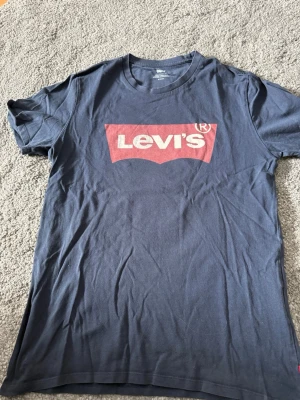 Levi's t-shirt  - Snygg mörkblå t-shirt från Levi's med den klassiska röda loggan tryckt på bröstet. T-shirten har rund halsringning och korta ärmar. Perfekt för en avslappnad och stilren look.