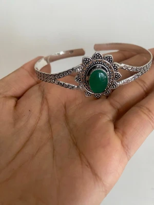 s925 sterling Silvrigt armband med grön sten - Snyggt armband i silverfärgad metall med en stor grön oval sten i mitten. Armbandet har ett detaljerat mönster runt stenen som påminner om en blomma och små pärldetaljer längs bandet. Perfekt för dig som gillar boho eller vintage-inspirerad stil. material: sterling silver pläterat s925 - justerbar