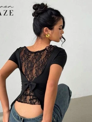 Svart topp med spets och rosett - Snygg svart topp från Siren Gaze med korta ärmar och tight passform. Baksidan har transparent spets och en dekorativ rosett. Materialet är troligtvis polyester och toppen har en feminin, croppad stil som framhäver midjan.