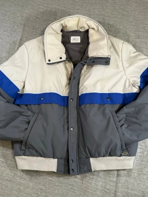 Vintage 90s Wrangler Puffer Jacket XL Made in Hong Kong Off White Blue Boxy Cropped Bomber - Vintage 90s Wrangler puffer jacket XL made in Hong Kong. Clean boxy bomber fit with off white upper, cobalt blue stripe and grey body. Lightweight insulation – perfect spring/fall layer, not heavy winter. Subtle light discoloration on collar (hard to see, noted for transparency).  Measurements laid flat: S2S 51 cm P2P 67.5 cm Length 67 cm Sleeve 70.5 cm  Proper 90s outdoor energy. Easy everyday vintage piece.