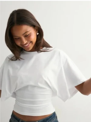 Vit croppad topp med vida ärmar - Säljer en vit croppad topp från H&M med vida, korta ärmar och en tight passform runt midjan. Perfekt att matcha med jeans eller kjol för en cool och avslappnad look. Materialet är mjukt och känns bekvämt mot huden.