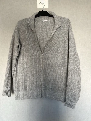 Grå cardigan  - Säljer en grå caru tröja från Dobber med dragkedja framtill och hög krage. Tröjan har långa ärmar och breda muddar vid ärmslut och nederkant. Perfekt för lager på lager och enkel att matcha med olika outfits.