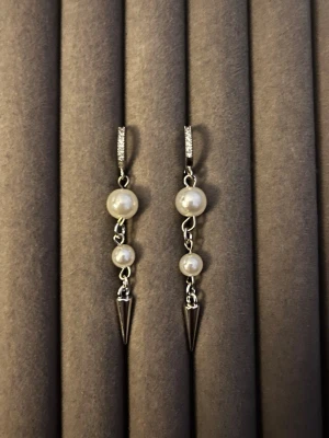 Silverörhängen med pärlor och spikes - Snygga örhängen i silverfärg med två vita pärlor och en spetsig spike-detalj längst ner. Örhängena har små gnistrande stenar på bygeln för extra bling. Perfekt accessoar för dig som gillar en mix av klassiskt och edgy.