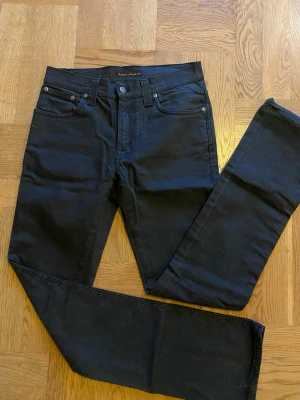 Svarta jeans från Nudie Jeans - Snygga svarta jeans från Nudie Jeans med klassisk femficksdesign och raka ben. Jeansen har diskreta sömmar och logga på bakfickan. Tillverkade i mjuk bomullsdenim med lite stretch för extra komfort.