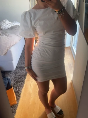Vit kort puffärmad klänning - Säljer en vit kort klänning med puffärmar och figurnära passform, den har även en öppen rygg. Så snygg klänning, perfekt till student och sommar!!