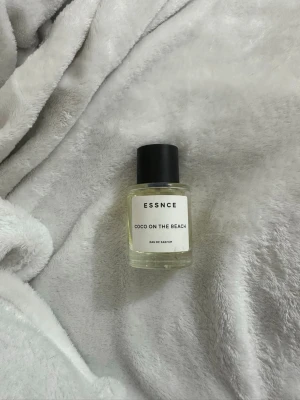 ESSNCE Coco On The Beach parfym - Fräsch parfym från ESSNCE med namnet Coco On The Beach. Flaskan är genomskinlig med en enkel vit etikett och svart lock. Doften är en Eau de Parfum och flaskan har en stilren, rund form i glas. Perfekt för dig som gillar minimalistisk design.