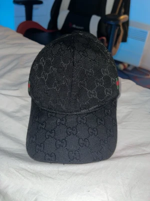 Svart keps med monogram, märket ser ni själva - Säljer en svart keps, märket ser ni själva med klassiskt GG-monogram över hela kepsen. På sidan finns en grön och röd rand som ger den en ikonisk touch. Kepsen har böjd skärm och är tillverkad i ett slitstarkt tygmaterial. (Priset är diskuterbart!!!)