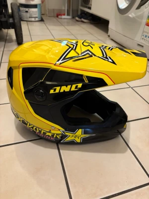 Rockstar Energy gul motocrosshjälm - Säljer en gul och svart motocrosshjälm från One med Rockstar Energy Drink-logga och stora stjärndetaljer. Hjälmen har en cool design med skärm framtill och tydliga grafiska mönster. Perfekt för dig som gillar action och vill sticka ut.