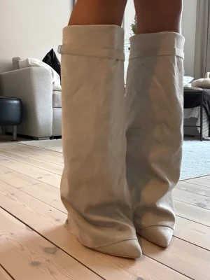 Beige fold over boots - Säljer ett par beige folded eller fold over boots med breda skaft och coola spänndetaljer upptill. Bootsens material ser ut som mjukt konstläder och de har en slouchy, avslappnad passform med spetsig tå. Klacken är ca 9 cm. Storlek 40 men små i storlek och passar bäst på någon med 39. Köpta från prettylittlething och i nyskick.