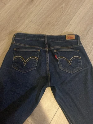 Mörkblå bootcut lågmidjade jeans från Levi's - Snygga mörkblå jeans från Levi's med klassiska gula sömmar och bootcut passform, Levi's ikoniska röda etikett på bakfickan vet inte vilken storlek dem är men jag brukar ha 34/36 i jeans så om du har de eller lite mindre så tror jag dem kommer passa bra 