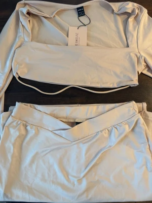 Beige set från Shein med lång ärm - Trendig beige body och kjol-set från Shein. Överdelen har långa ärmar, fyrkantig urringning och smal passform med band under bysten. Kjolen har omlott-look och bred linning. Perfekt för dig som gillar stilrena och moderna plagg.