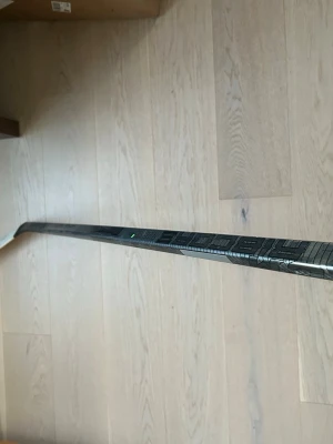 Svart hockeyklubba 55 Flex P90TM - Säljer en svart hockeyklubba med 55 Flex och P90TM-blad. Klubban har en modern design med mönster längs skaftet och är tillverkad i kompositmaterial. Perfekt för dig som vill ha bra kontroll och känsla på isen.
