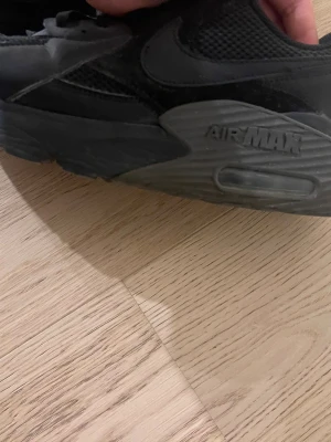 Svarta Nike Air Max sneakers - Säljer ett par helsvarta Nike Air Max sneakers med klassisk mesh och skinnpaneler. Skorna har tydlig Air Max-detalj på sulan och snörning framtill. Perfekta för dig som gillar stilrena och sportiga sneakers.