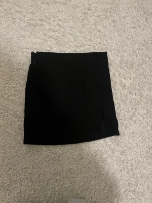 Svart kortkjol i bomull - Enkel och stilren svart kortkjol i mjukt bomullsmaterial. Kjolen har en rak passform och dragkedja i sidan för enkel på- och avtagning. Perfekt att matcha med en crop top eller oversized tröja.