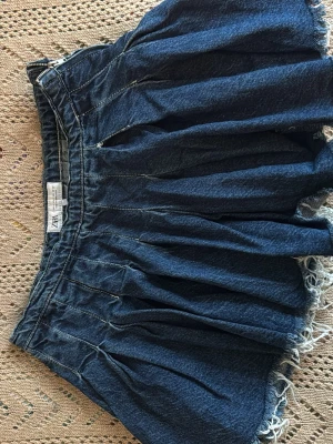 Blå jeanskjol från Zara - Snygg blå jeanskjol från Zara med kort längd och råa fransade kanter. Kjolen har en avslappnad passform och är gjord i denim med tydliga sömmar som ger en cool look. Perfekt för dig som gillar en trendig och avslappnad stil.