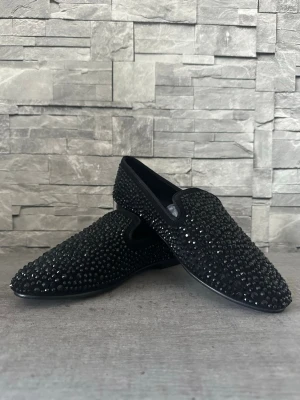 Giuseppe Zanotti Design loafers – svart med stenar - Säljer ett par svarta loafers från Giuseppe Zanotti täckta med svarta nitar över hela skon. Skorna har en klassisk slip-on design och en låg sula. Perfekta för dig som vill sticka ut med en edgy och lyxig stil. ✨