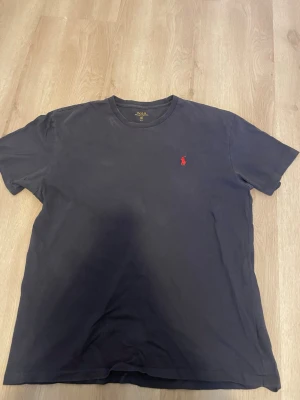 Svart t-shirt från Polo Ralph Lauren - Klassisk svart t-shirt från Polo Ralph Lauren med rund hals och den ikoniska röda logotypen broderad på bröstet. Tillverkad i mjuk bomull som känns skön mot huden. Perfekt basplagg för en clean och stilren look. Pris kan diskuteras.