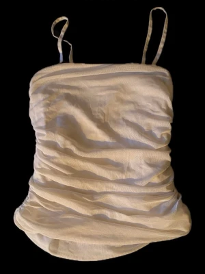 Vit rynkad linnetopp med smala band❕ - Snygg vit linnetopp med smala axelband och rynkade detaljer längs sidorna. Toppen har en omlottliknande form och är perfekt för en fräsch och stilren look. Passar till många olika outfits och är lätt att matcha🎐