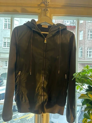 Grön cardigan från Moncler - Snygg olivgrön cardigan från Moncler med dragkedja framtill, huva med snörning och ribbade ärmar. Jackan har släta paneler fram och fickor med dragkedja. Perfekt för en casual streetstyle-look. Priset är inte hugget i sten