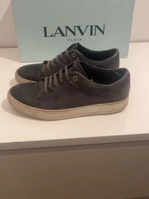 Svarta sneakers från Lanvin - Snygga svarta sneakers från Lanvin med ovandel i mocka och tåparti i blankt läder. Skorna har klassisk låg profil, vita sulor och matchande svarta skosnören. Perfekta för dig som gillar stilrena och exklusiva sneakers. Stl är mer som 43