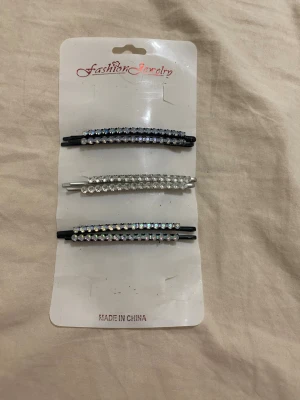 Glittriga hårspännen med strass - Tre hårspännen i metall dekorerade med gnistrande strasstenar i silver och regnbågsskimrande nyanser. Två spännen är svarta och ett är silverfärgat. Perfekta för att ge frisyren extra bling och stil.