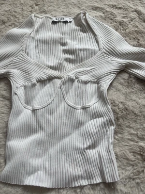 Vit ribbad topp från NA-KD - Trendig vit ribbad topp från NA-KD med markerade sömmar över bysten och v-ringad hals. Långärmad och figurnära passform som ger en snygg siluett. Perfekt att styla med jeans eller kjol för en cool look.