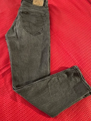 Svarta Lee jeans med rak passform storlek (29)  - Säljer ett par svarta Lee jeans med klassisk rak passform och femficksmodell. Jeansen har en snygg tvättad look och är tillverkade i slitstarkt denimtyg. Perfekta för dig som gillar en tidlös och avslappnad stil.