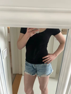 Ljusblå jeansshorts - Säljer ett par ljusblå jeansshorts med råa, fransiga kanter och klassisk femficksdesign. Shortsen har en avslappnad passform och är perfekta för varma dagar. Passar dig som gillar en casual och trendig stil.