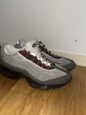 Nike Air Max 95 grå/vinröd sneakers - (Priset kan diskuteras) köpta för runt 2000 Knappt använda.  Nike Air Max 95 sneakers i grått och vinrött med svarta detaljer. Ovandel i mesh och mocka, klassisk vågig design och synlig Air Max-dämpning i sulan. Snygga snörningar med vinröda och svarta band. Perfekta för dig som gillar retrostil och streetwear.