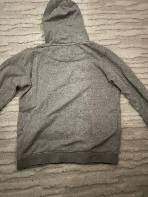 Grå hoodie från Lyle & Scott - Snygg grå hoodie från Lyle & Scott Junior med klassisk huva och mjukt material. Perfekt för en avslappnad stil och har den ikoniska gula loggan på bröstet. Passar dig som gillar enkel och stilren design.