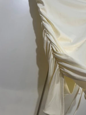 Krämvit oneshoulder topp med snörning - Säljer en krämvit oneshoulder topp med snygg drapering och snörning längs sidan. Toppen har en asfin asymmetrisk skärning och är gjord i ett mjukt, stretchigt material som känns skönt mot huden. Perfekt för dig som vill sticka ut lite extra.