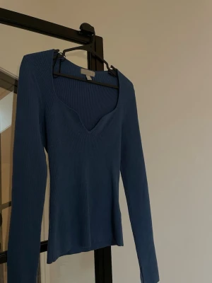 Blå ribbstickad tröja med v-ringning - Snygg blå ribbstickad tröja med djup v-ringning och långa ärmar. Tröjan har en smickrande passform och är tillverkad i ett mjukt, stretchigt material. Perfekt att styla med jeans eller kjol för en trendig look. ( sticks ej ) 