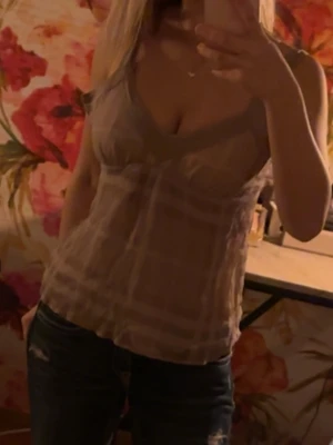 Beige rutig linne med v-ringning - Säljer ett beige linne med rutigt mönster och djup v-ringning. Toppen är ärmlös och har en loose passform, perfekt för varma dagar. Passar dig som gillar en enkel men ändå trendig stil.