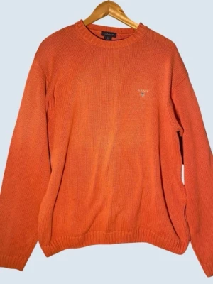 Orange stickad tröja från Gant XL - Säljer en orange stickad tröja från Gant med rund halsringning och diskret broderad logga på bröstet. Tröjan har långa ärmar och ribbade muddar vid ärmslut och nederkant. Perfekt för dig som gillar klassisk och enkel stil.