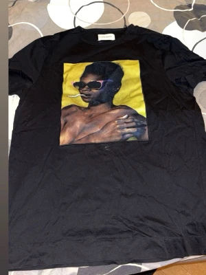 Svart t-shirt från Limitato med tryck -  svart t-shirt från Limitato med ett stort färgstarkt tryck framtill i samarbete med Riocam. T-shirten har rund halsringning och klassisk passform. Perfekt för dig som vill sticka ut med en unik design.