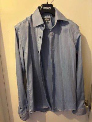 Ljusblå skjorta från Eton - Klassisk ljusblå skjorta från Eton med lång ärm och knappar framtill. Skjortan har en stilren krage och är tillverkad i bomull för en bekväm känsla. Perfekt till både jeans och kostymbyxor.