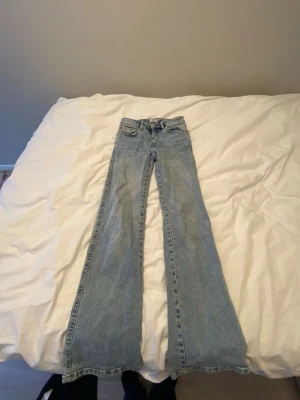 Ljusblå utsvängda jeans från 157 - Säljer ett par ljusblå jeans från 157 med utsvängda ben och klassisk femficksmodell. Jeansen har snygga detaljer på bakfickorna med knappar och en patch med logga i midjan. Perfekta för dig som gillar retrostil och relaxed fit.