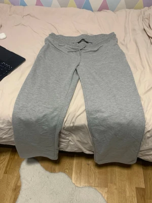 Gråa mjukisbyxor med dragsko - Säljer ett par klassiska gråa mjukisbyxor med dragsko i midjan och raka ben. Perfekta för chill dagar hemma eller när du vill vara extra bekväm. Tillverkade i mjukt bomullsmaterial som känns skönt mot huden.
