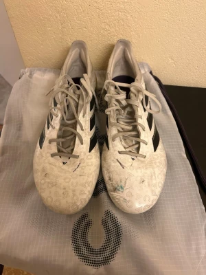  Adidas Copa pure 3 AG - Säljer ett par vita Adidas fotbollsskor med svarta ränder och unikt mönster på ovandelen. Skorna har gula dobbar och är tillverkade i syntetmaterial. Perfekta för dig som vill sticka ut på planen med stilrena och sportiga skor.