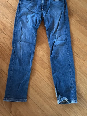 Blå jeans från Jack & Jones Regular/Clark 29/32 - Säljer ett par klassiska blå jeans från Jack & Jones, modell Regular/Clark. Jeansen har rak passform, fem fickor och är tillverkade i slitstark denim. Perfekta för en avslappnad och stilren look.