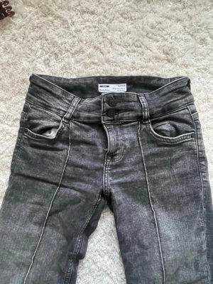 Grå utsvängda jeans från Bershka - Säljer ett par grå jeans från Bershka med utsvängda ben och markerade sömmar framtill. Jeansen har dubbla knappar i midjan och klassiska fickor både fram och bak. Perfekta för dig som gillar en trendig och avslappnad stil.
