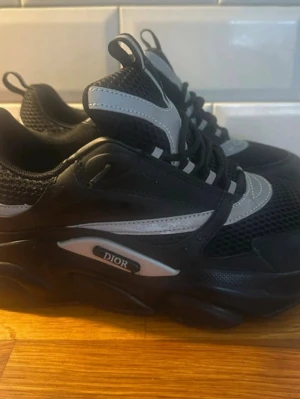 Svarta sneakers med mesh och läder - Snygga svarta sneakers med grå och vita detaljer. Ovandelen är i mesh och läder för en sportig vibe. Tjock sula och klassisk snörning. Perfekta för dig som vill ha en exklusiv och trendig look. Stl 42 men är små i storleken så jag skulle säga 41. 