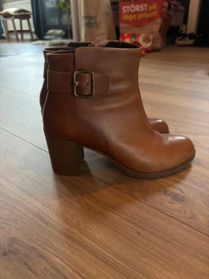 Bruna vagabond stövlar - Snygga bruna stövletter i slätt läder från Vagabond, med bred klack och dekorativt spänne på sidan. Klassisk rund tå och dragkedja på insidan för enkel påtagning. Perfekta till jeans eller kjol för en trendig look.