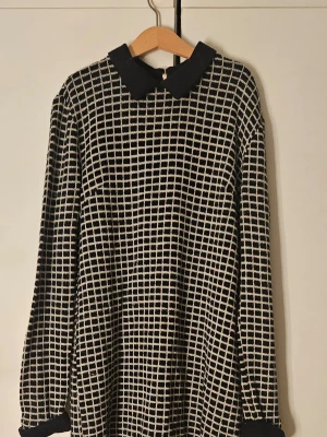 Svartvit rutig vintage klänning - Mönstrad svartvit klänning med långa ärmar. Klänningen är figursydd och är tillverkad i ett mjukt, stickat material. Perfekt för dig som gillar grafiska mönster och en avslappnad stil.