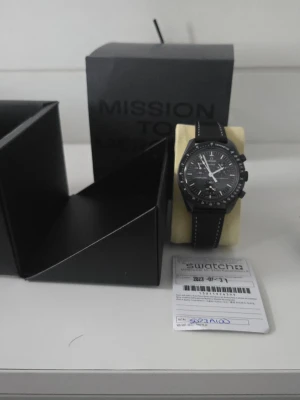 Swatch x Omega Mission to Mercury klocka -  Moonswatch in good condition. I’ve maintained this well, recently replacing the battery. The crystal and case show minor surface marks typical of light wear, but nothing significant.  ​Note on Straps: I no longer have the original velcro strap, but I’ve included two significantly better upgrades: a Wristbuddys rubber strap 600 sek and a genuine leather strap. ​Includes: Watch, Box, Warranty, and two premium straps *Note* the chronograph function does not work but the watch works fine other wise