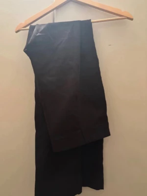 Svarta raka kostymbyxor - Snygga svarta kostymbyxor med rak passform och klassisk design. Perfekta för en stilren look och enkla att matcha med skjorta eller t-shirt. Byxorna har pressveck och är tillverkade i ett slätt tyg som ger en dressad känsla.