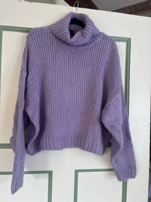 Ljuslila stickad polotröja - Mysig stickad polotröja i ljuslila med oversized passform och breda ärmar. Tröjan har ribbstickade muddar vid ärmslut och nederkant samt en hög, tjock polokrage. Perfekt för kalla dagar och enkel att styla till jeans eller kjol. Liten i storleken mer som S 