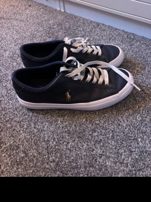 Marinblåa Polo Ralph Lauren sneakers - Snygga marinblå sneakers från Polo Ralph Lauren med vit sula och vita skosnören. Skorna har en klassisk låg modell. Storlek 39